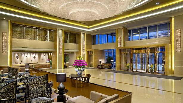 A spacious lobby with a high ceiling, large windows, and a central seating area with a table and chairs. - Expo Center Hotel  (Jinhua)