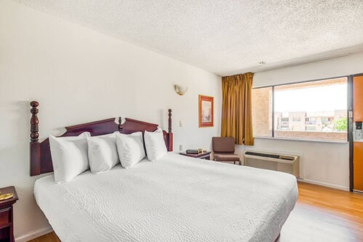 Ein Hotelzimmer mit einem großen Bett, einem Sessel, einem Fenster mit Vorhängen und einem Wandheizkörper.