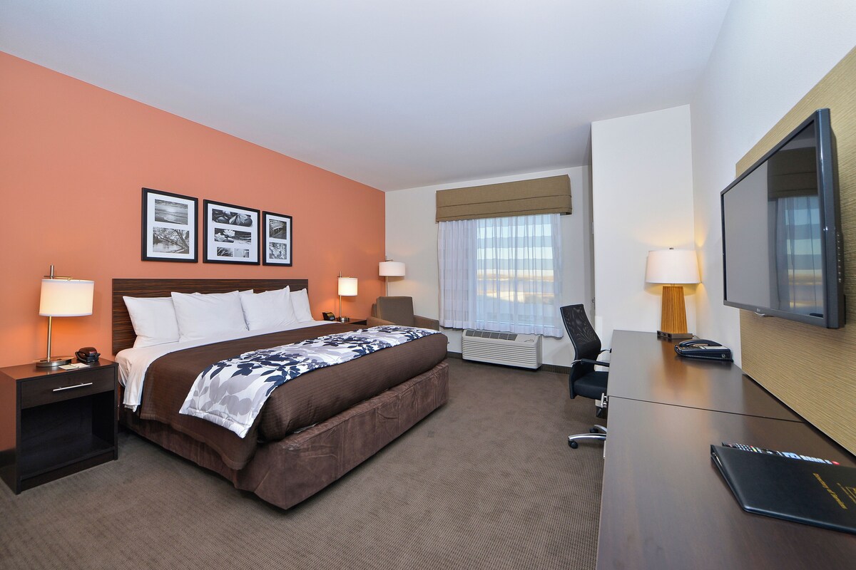 A hotel room with a bed, bedside tables, a desk, a chair, a television, and framed pictures on the wall.