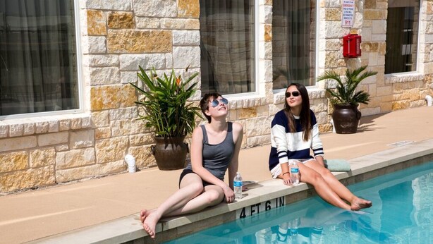 Two people sitting by a pool with stone walls and potted plants. - Sleep Inn & Suites Austin Northeast (Austin)
