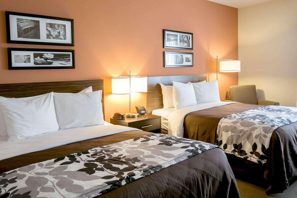 A hotel room with two beds, a nightstand, a lamp, and framed pictures on the wall.