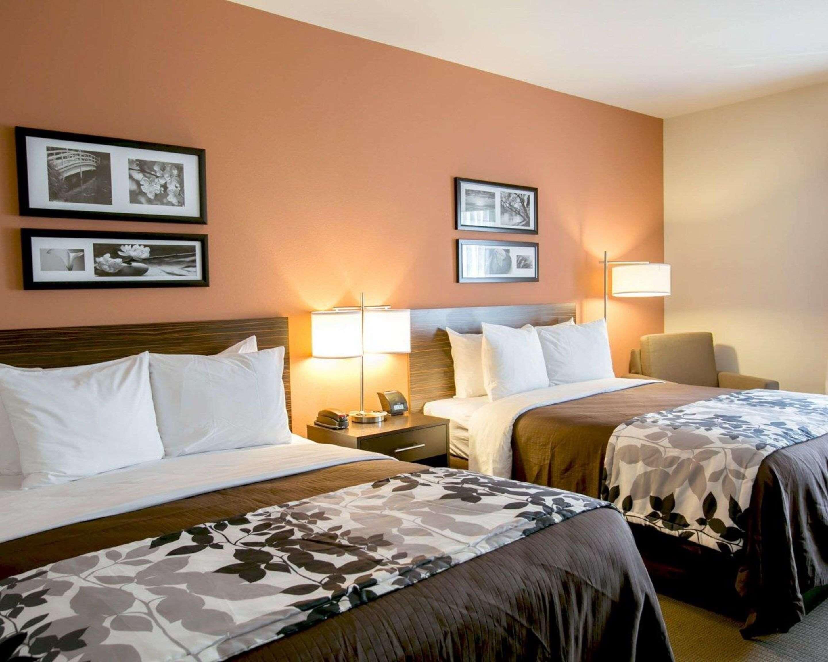 A hotel room with two beds, a nightstand, a lamp, and framed pictures on the wall.