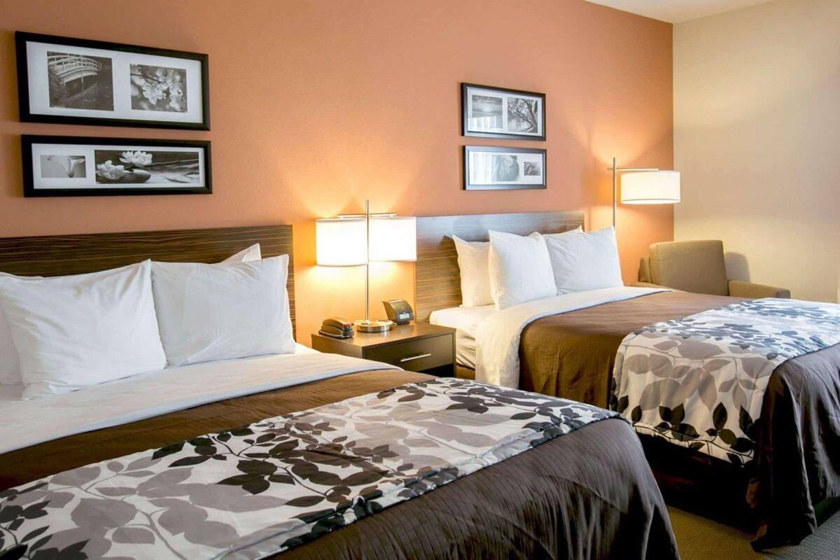 A hotel room with two beds, a nightstand, a lamp, and framed pictures on the wall.
