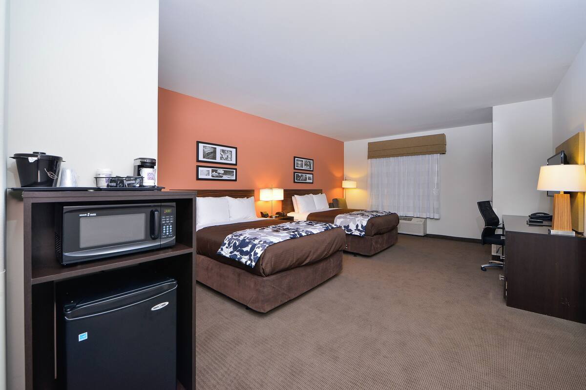 A hotel room with two beds, a microwave, a mini-fridge, a desk, and a lamp.