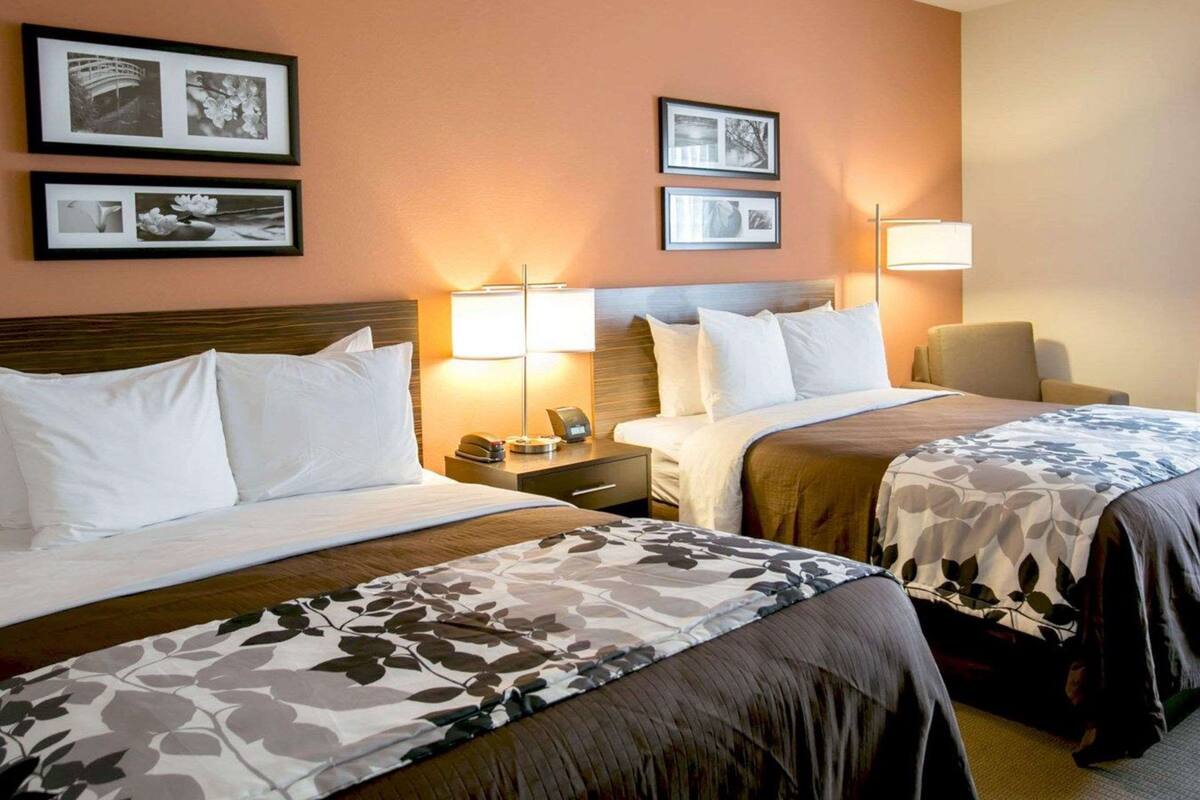 A hotel room with two beds, a nightstand with a lamp, and framed pictures on the wall.