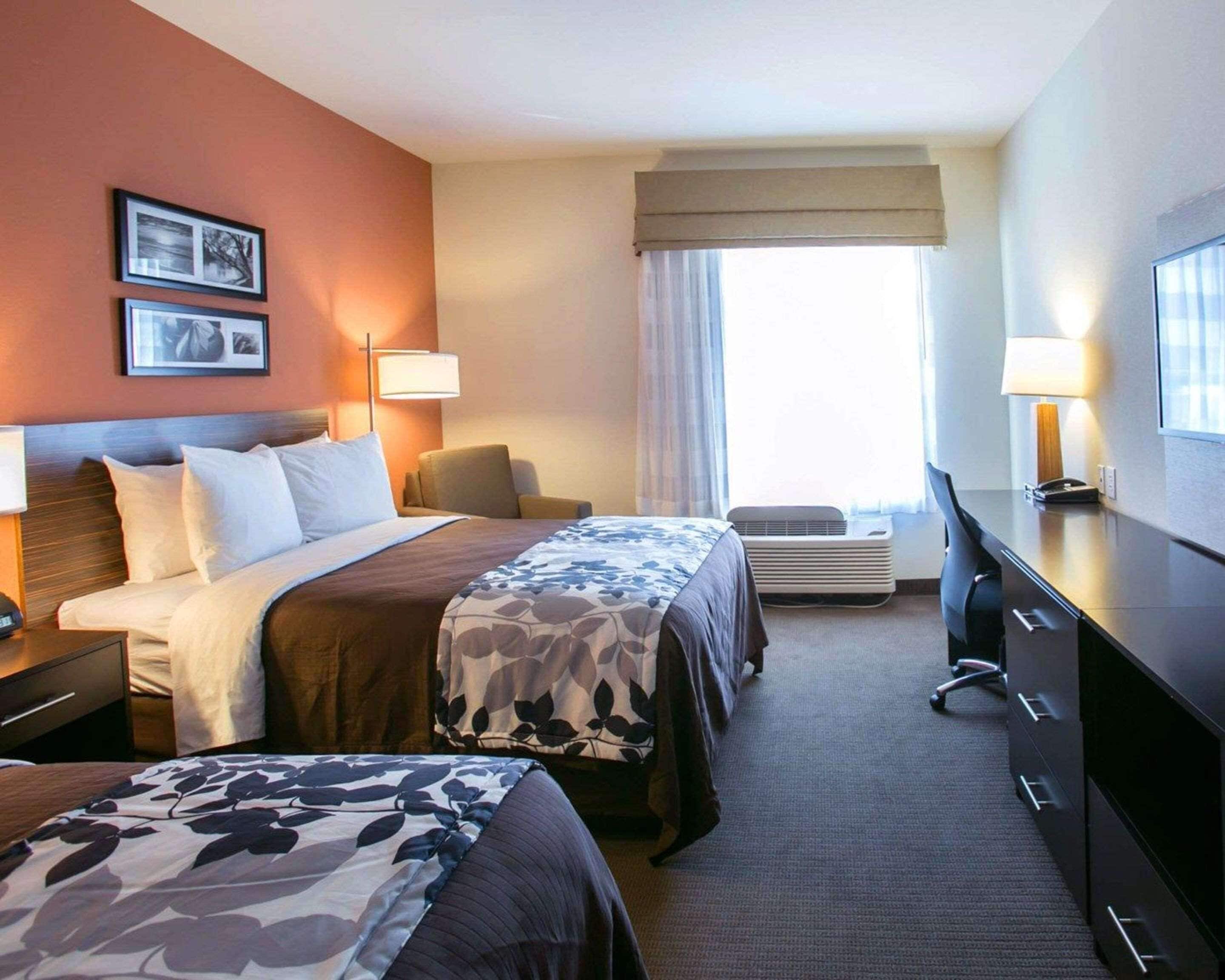 A hotel room with two beds, a desk, a chair, and a television.