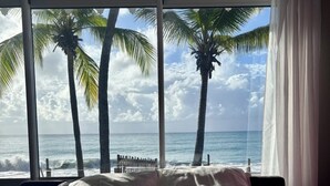 Ein Bett mit weißer Bettwäsche und Blick auf das Meer durch große Fenster.