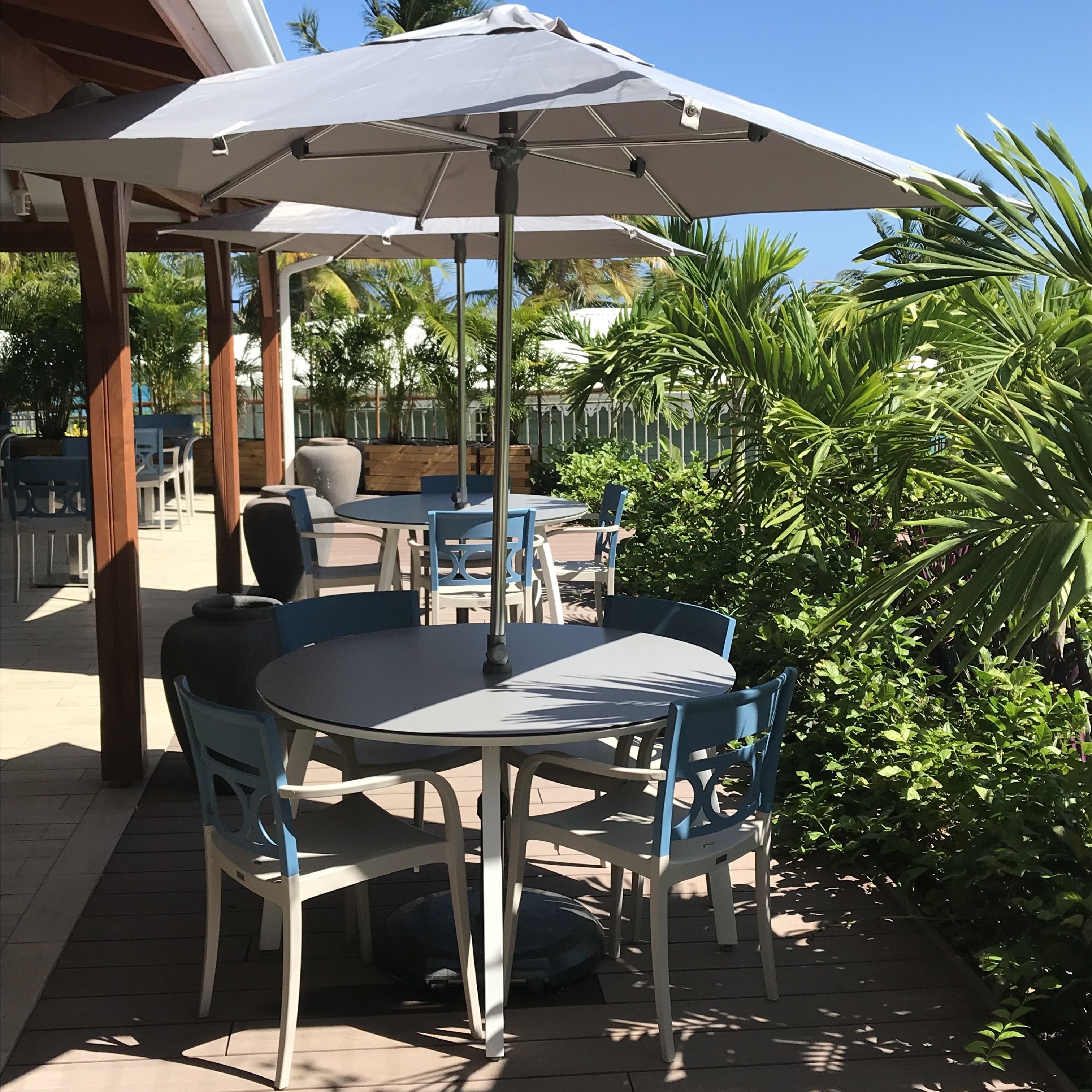 Une terrasse extérieure avec une table ronde et des chaises, un grand parasol et de la verdure tout autour.