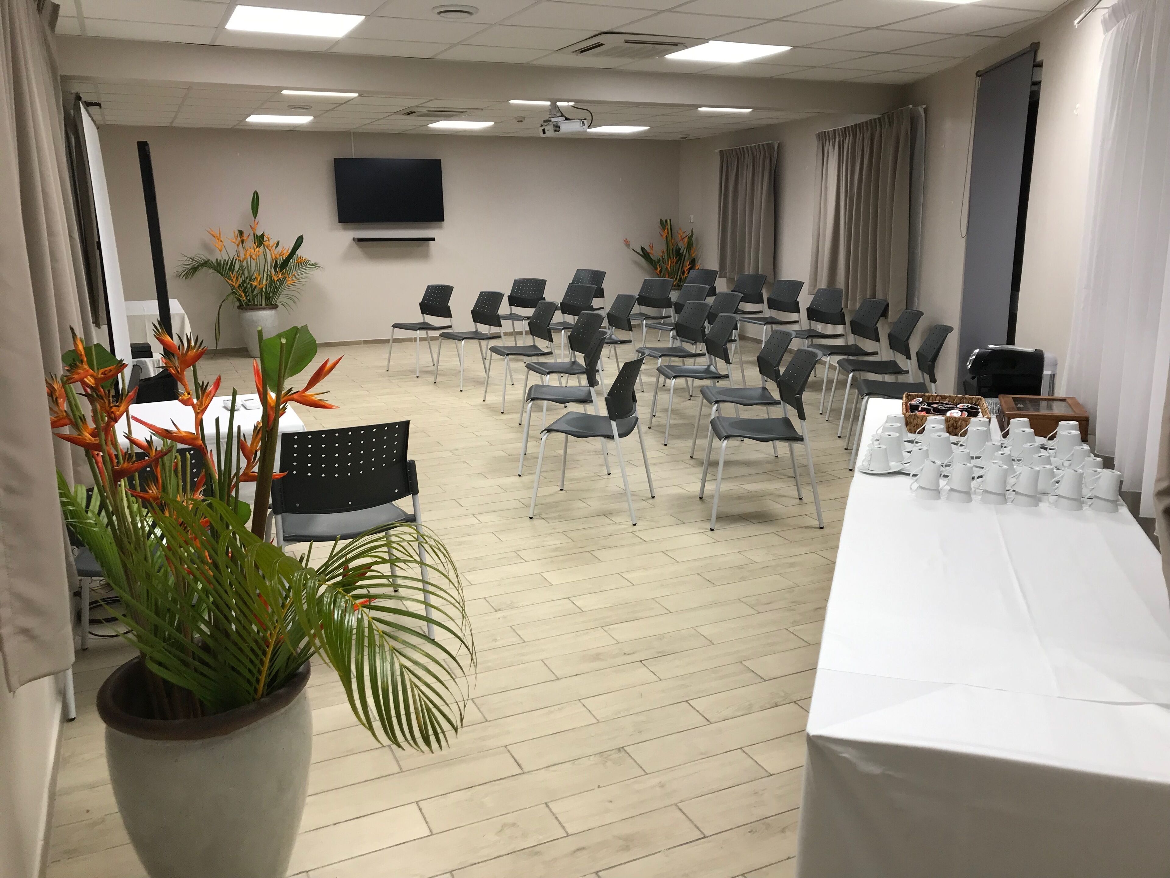 A conference room with rows of chairs, a projector screen, and a table with white cups.