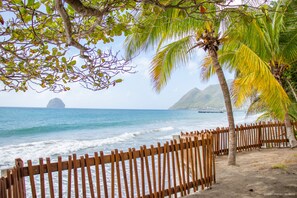 A wooden fence, palm trees, and a view of the ocean with a distant island. - Diamant les Bains Résidence Hôtelière (Le Diamant)