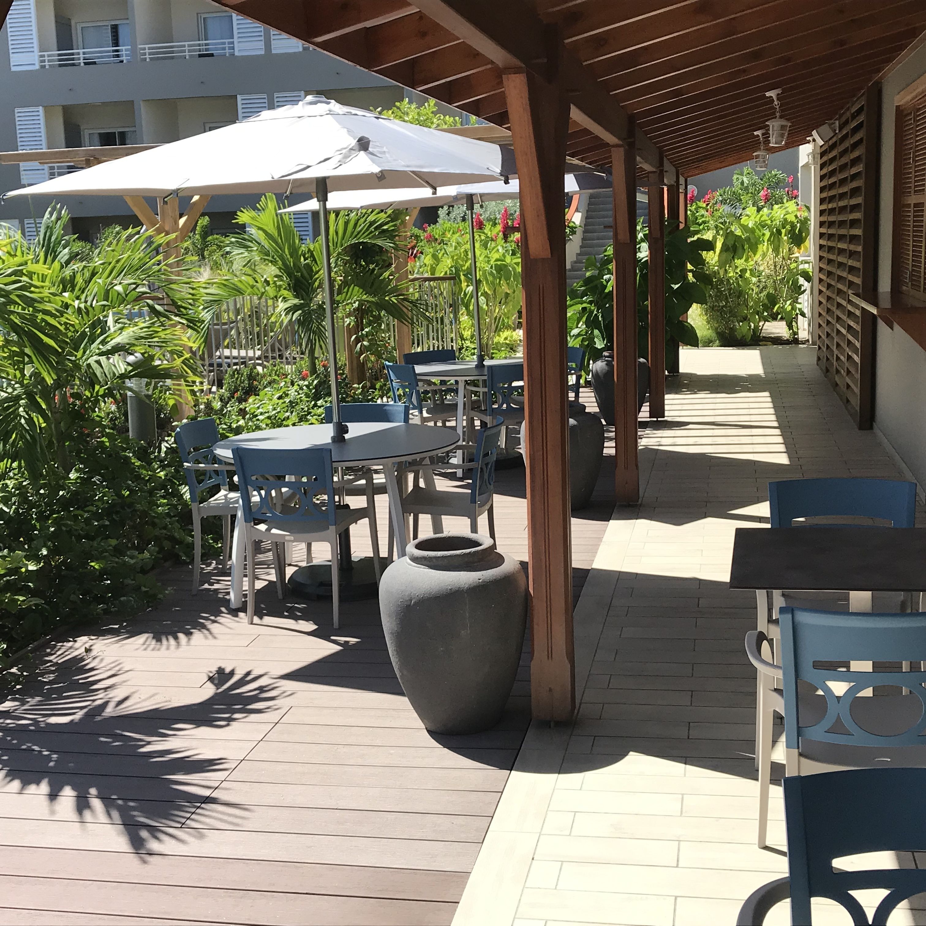 Ein Patio im Freien mit Tischen, Stühlen, Sonnenschirmen und Topfpflanzen.