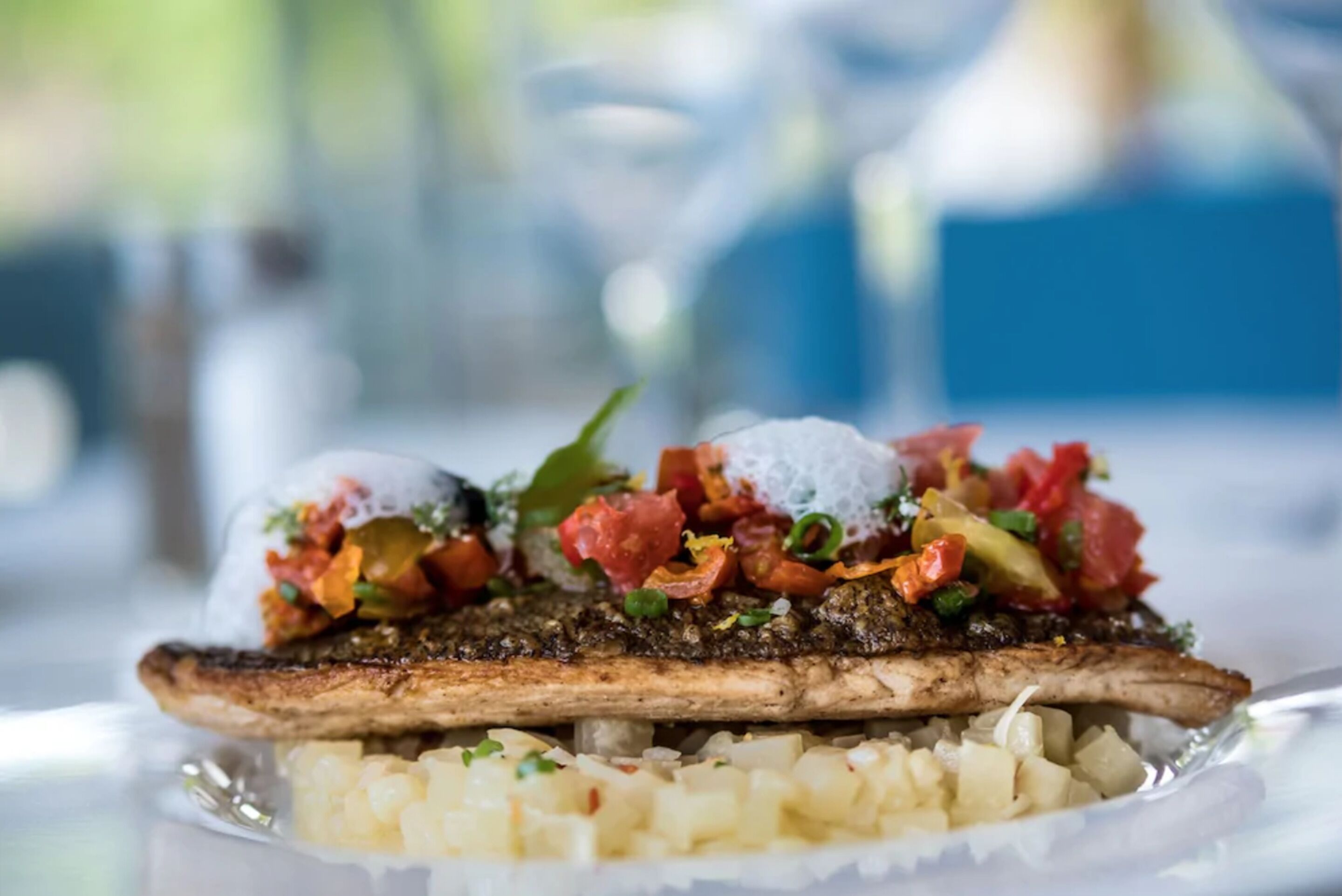 Un plato con un pescado a la parrilla, cubierto con una salsa colorida y patatas en cubos.