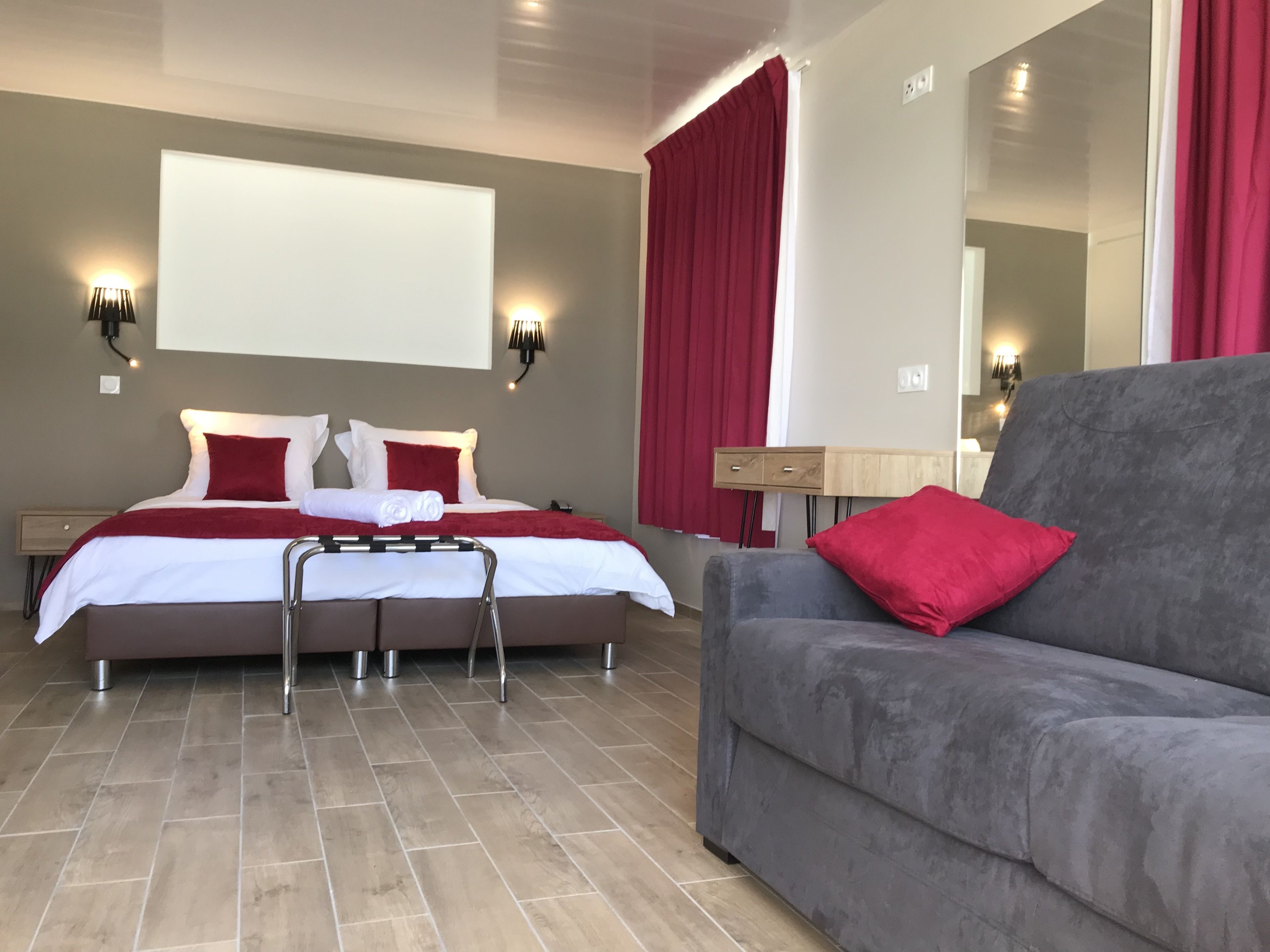 Une chambre d’hôtel moderne avec un lit, un canapé gris et un grand miroir.