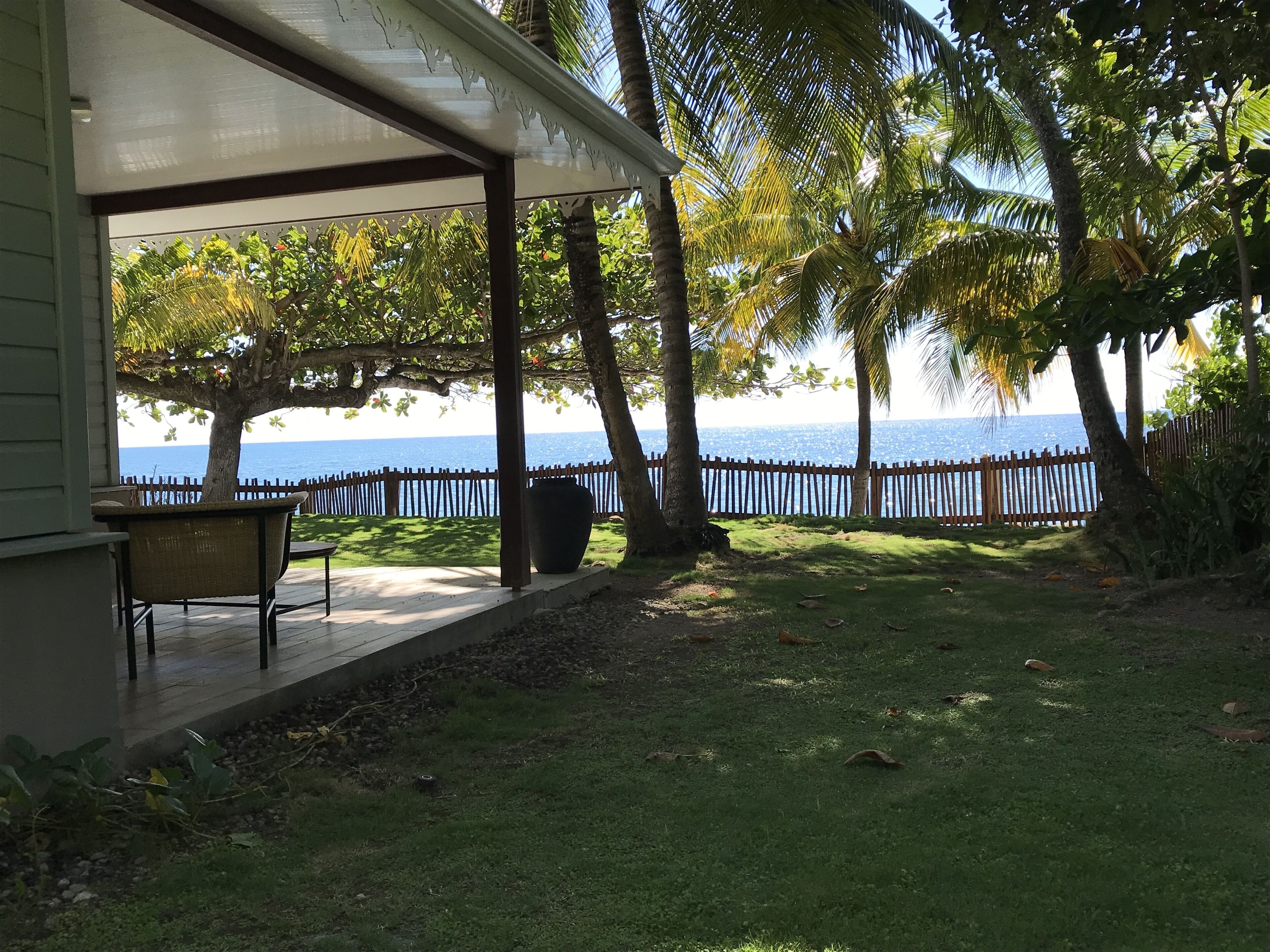 A covered patio with a view of the sea, a wooden fence, and a grassy area.
