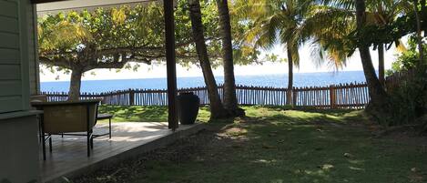 A covered patio with a view of the sea, a wooden fence, and a grassy area.
