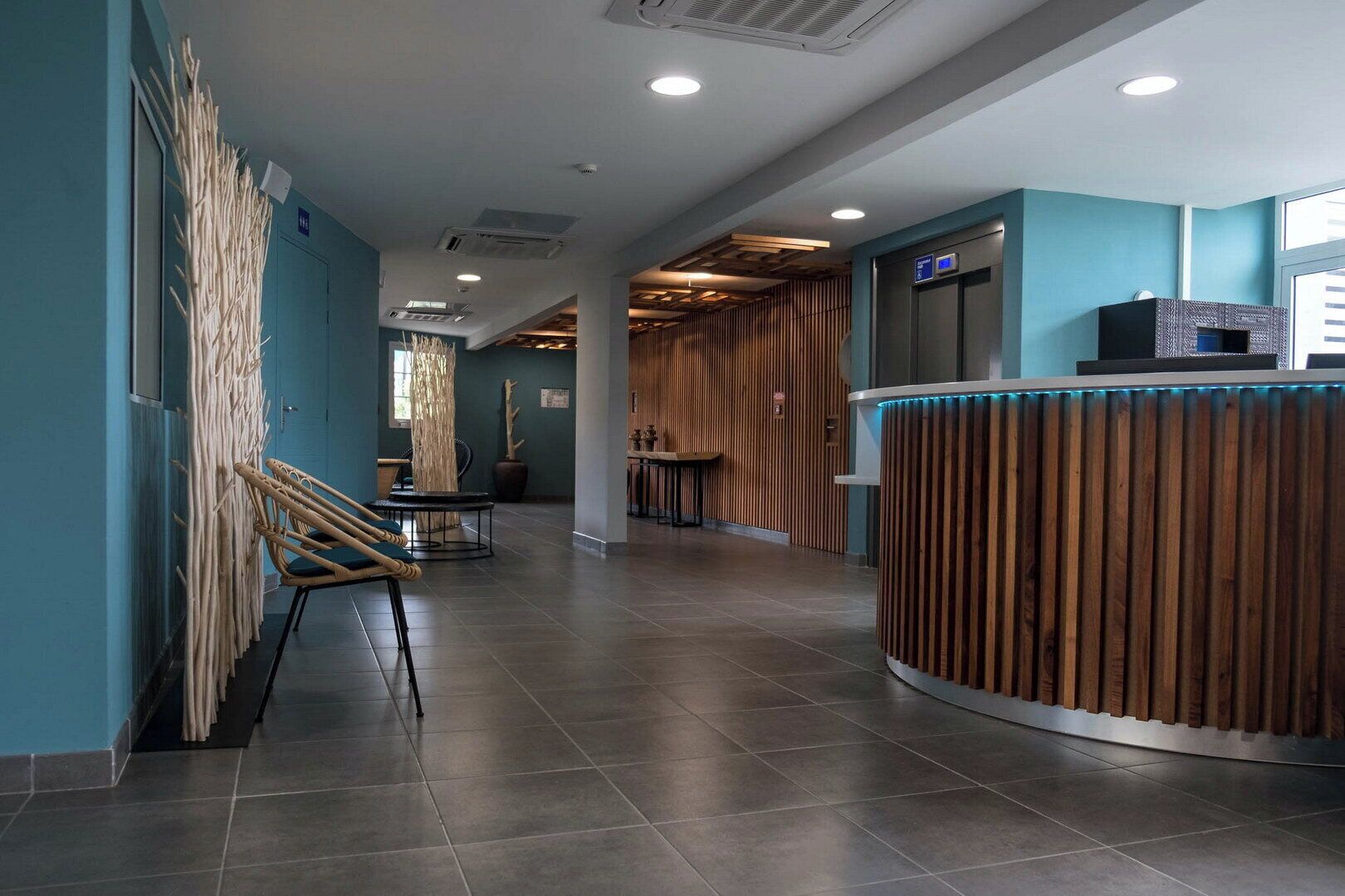 A modern hotel lobby with a reception desk, seating area, and a staircase.