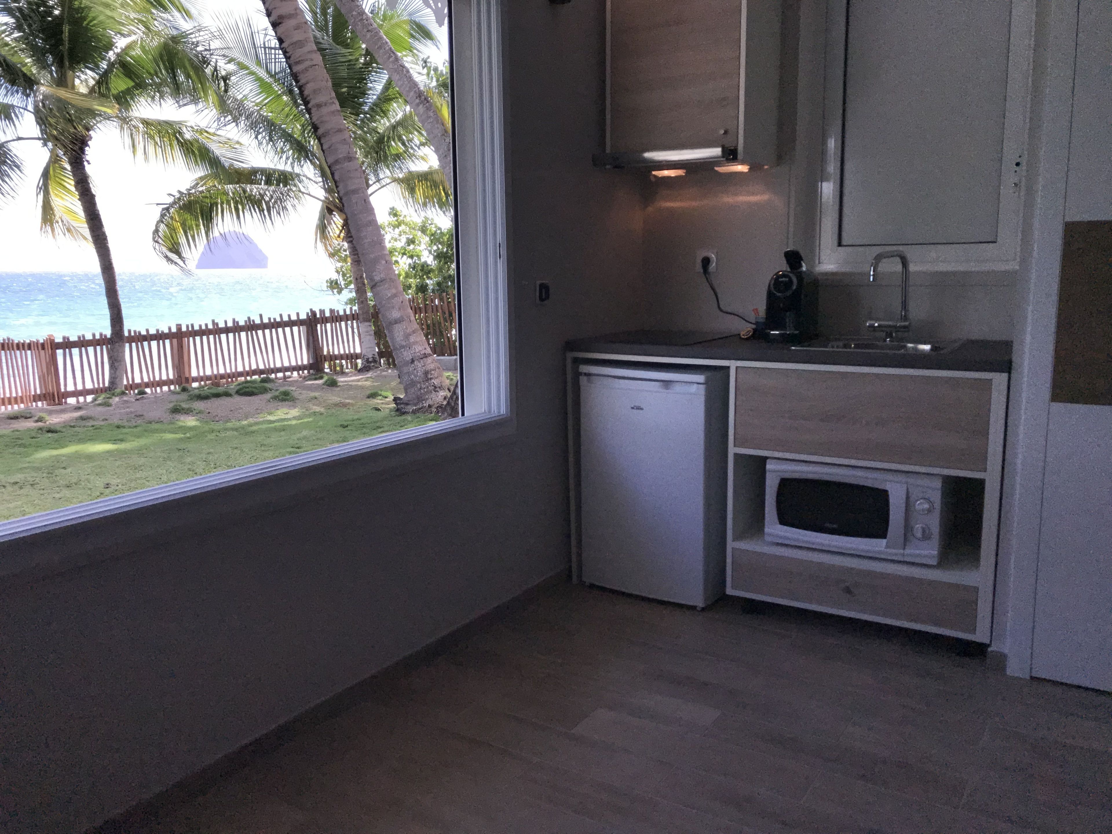 Cocina compacta con vista al océano, un refrigerador pequeño, un microondas y una cafetera en la encimera.