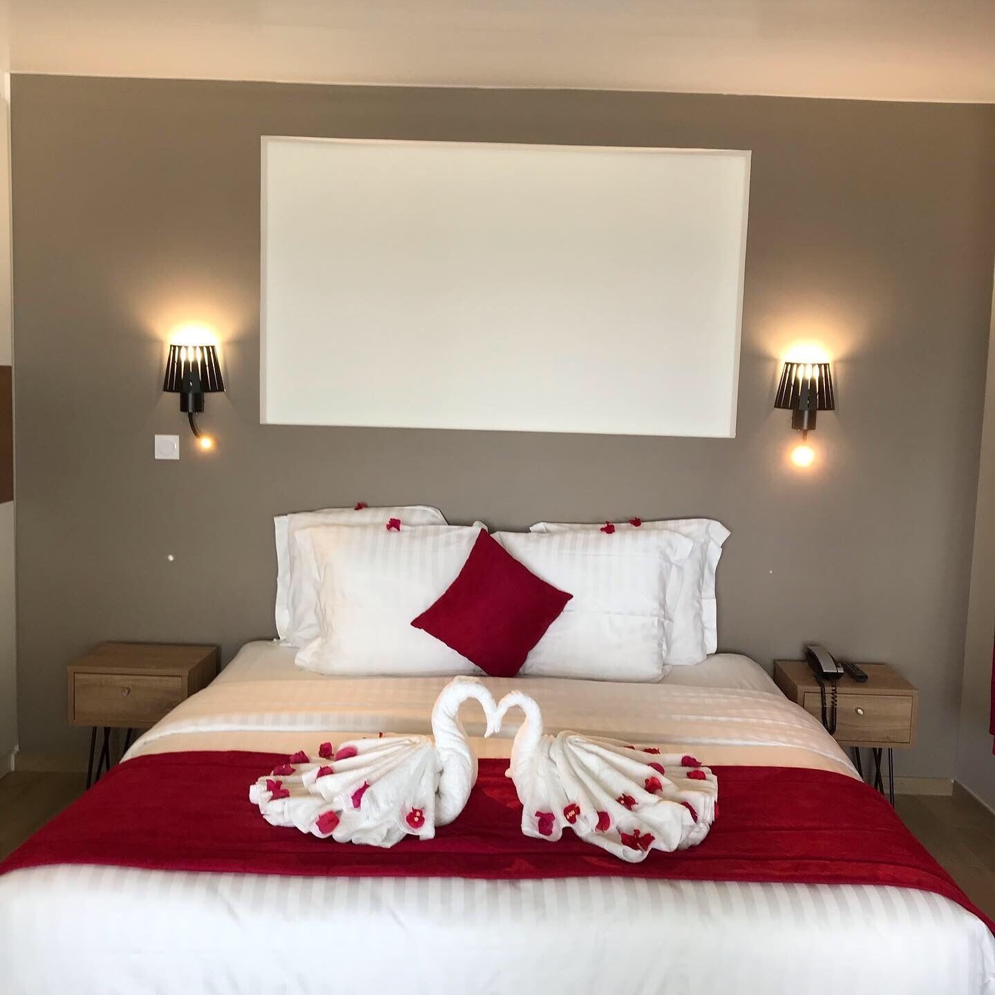 A hotel room with a large bed, two bedside tables, a wall-mounted light fixture, and a blank wall above the bed.