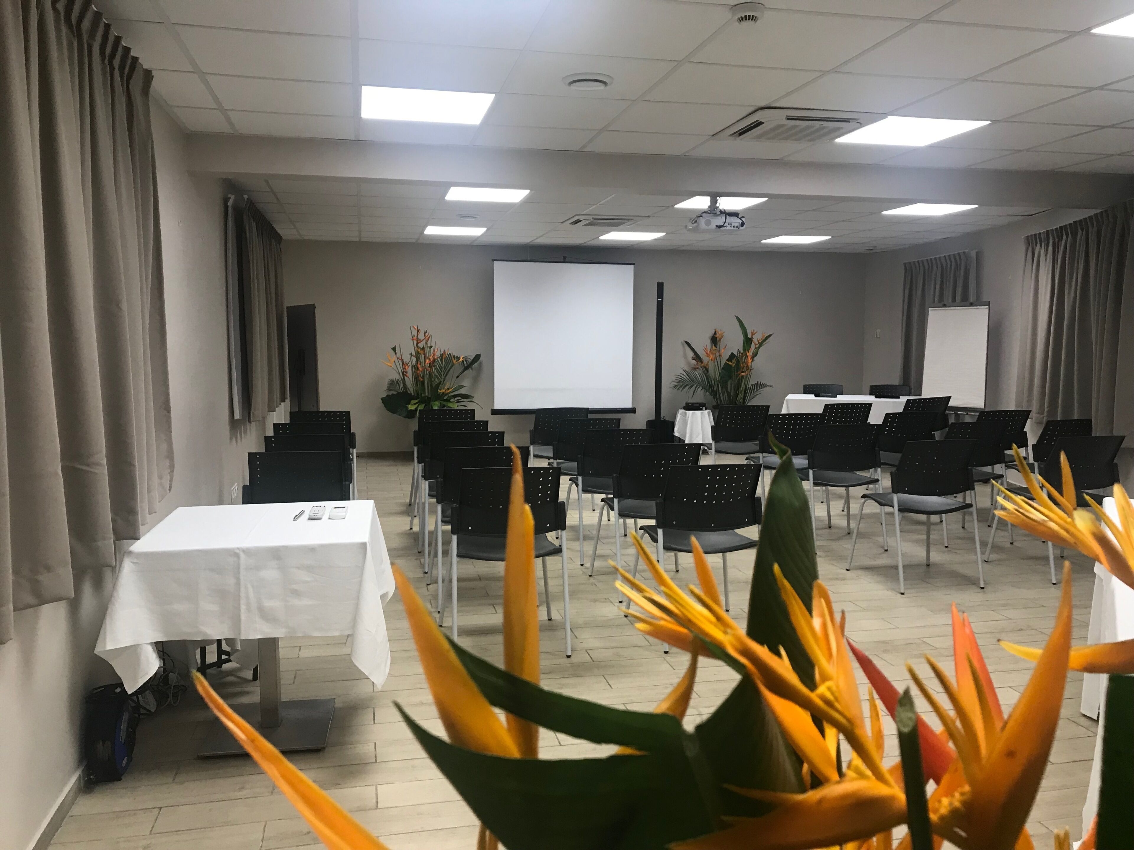 Un salón de conferencias con filas de sillas negras, una pantalla de proyección blanca y una pizarra.
