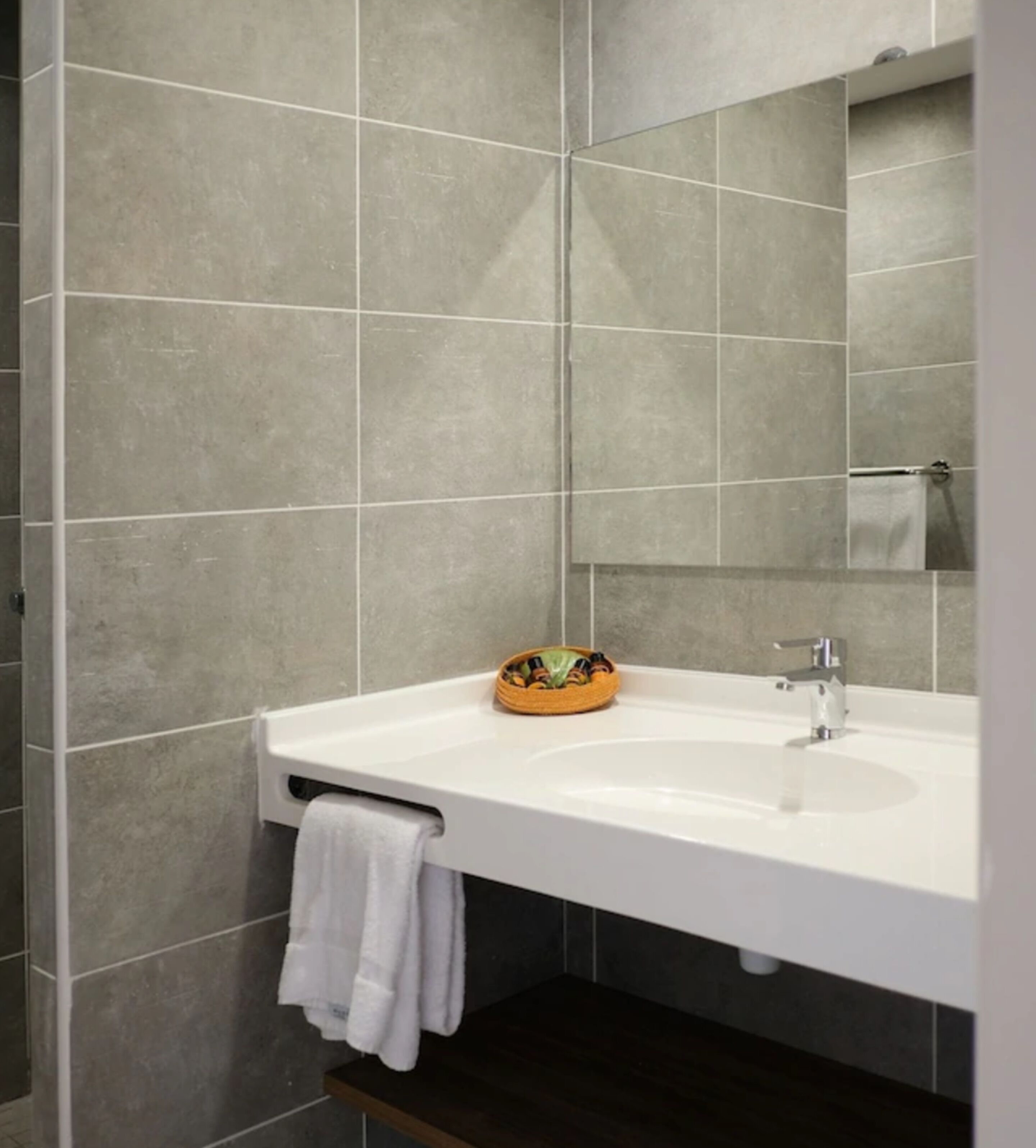 Un baño con un lavamanos blanco, un espejo y paredes revestidas de baldosas grises.