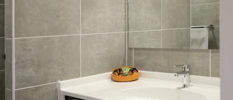 Un baño con un lavamanos blanco, un espejo y paredes revestidas de baldosas grises.