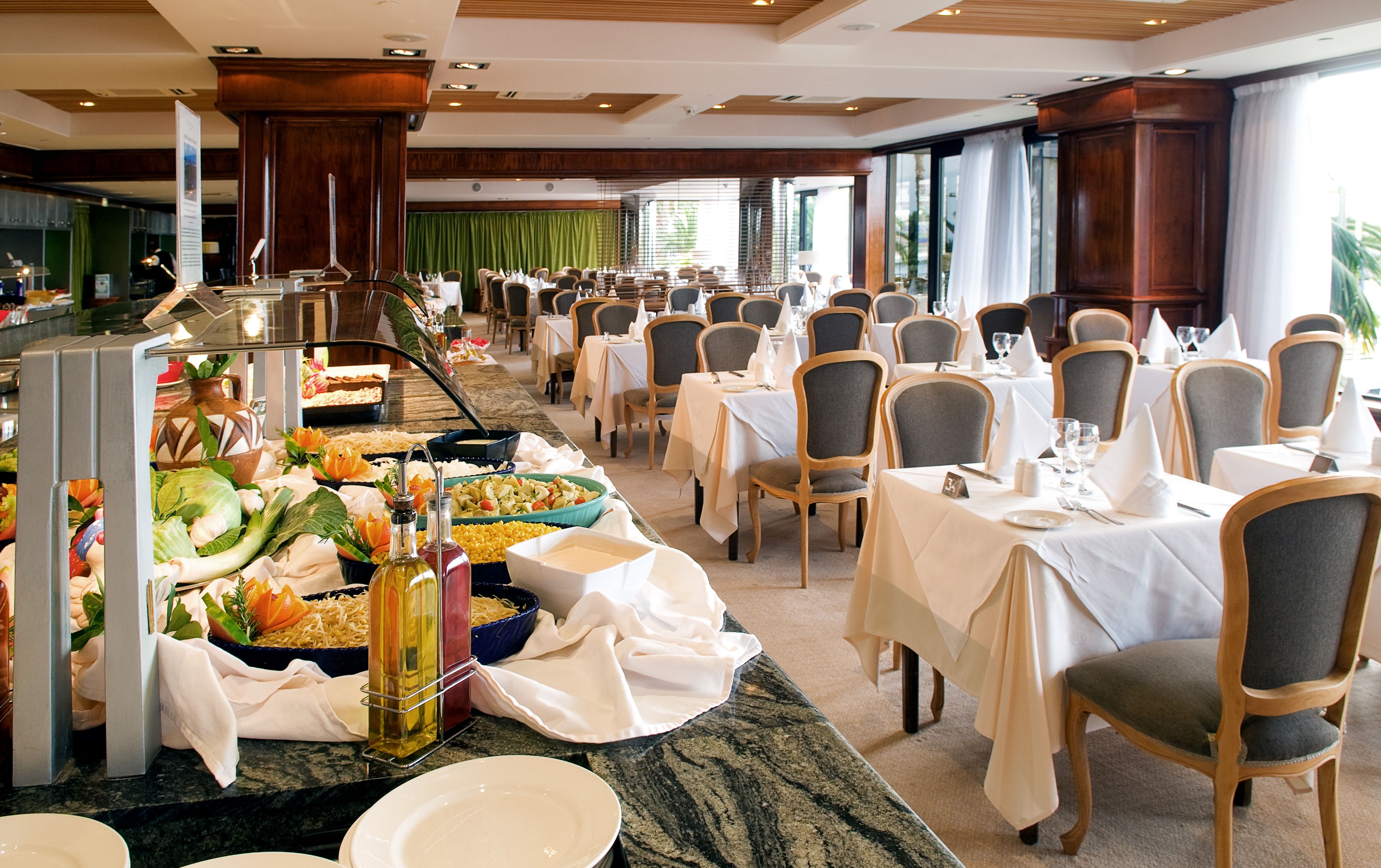 Un buffet proposant une variété de plats et de boissons, disposés sur un comptoir en marbre, avec des chaises et des tables préparées pour le repas.
