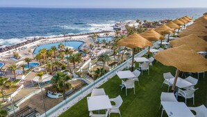 Un resort con piscina, playa y sombrillas de paja.