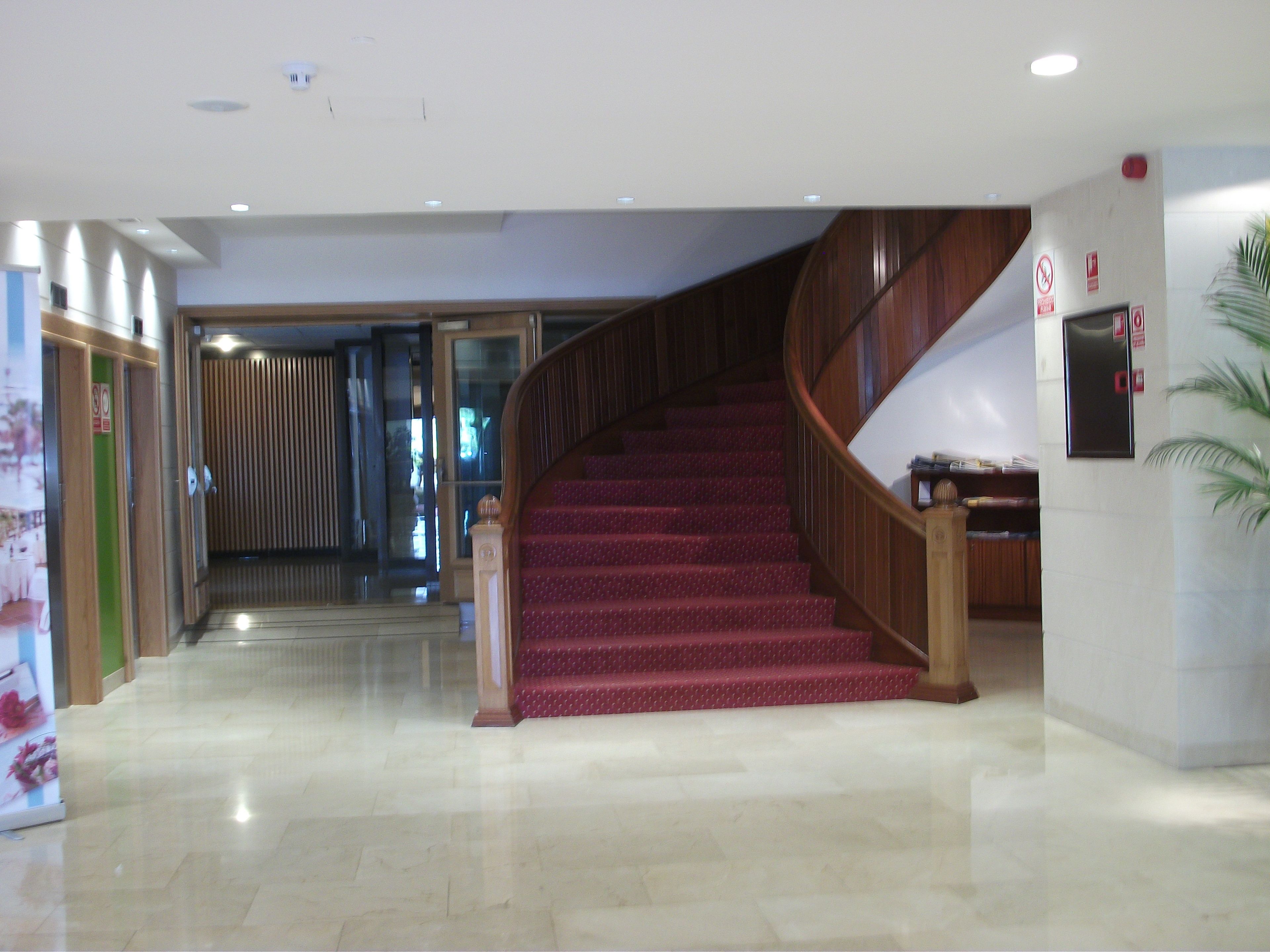 Eine Hotelhalle mit Marmorboden, einer Holztreppe mit rotem Teppich und einer Glastür zu einem weiteren Raum.