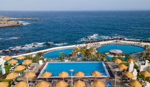 Un resort con una piscina grande, otra más pequeña y una zona de playa con sombrillas.
