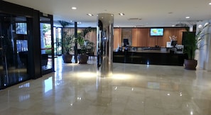 Um hall moderno com balcão de recepção, plantas grandes em vasos e piso lustroso.