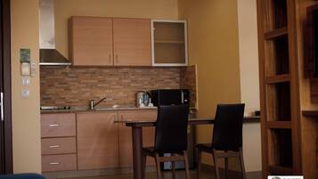 A compact kitchen with wooden cabinets, a microwave, and a coffee maker. There are two chairs and a table.