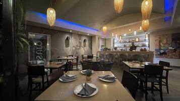A restaurant with tables set for dining, a bar area with bottles, and hanging wicker light fixtures.
