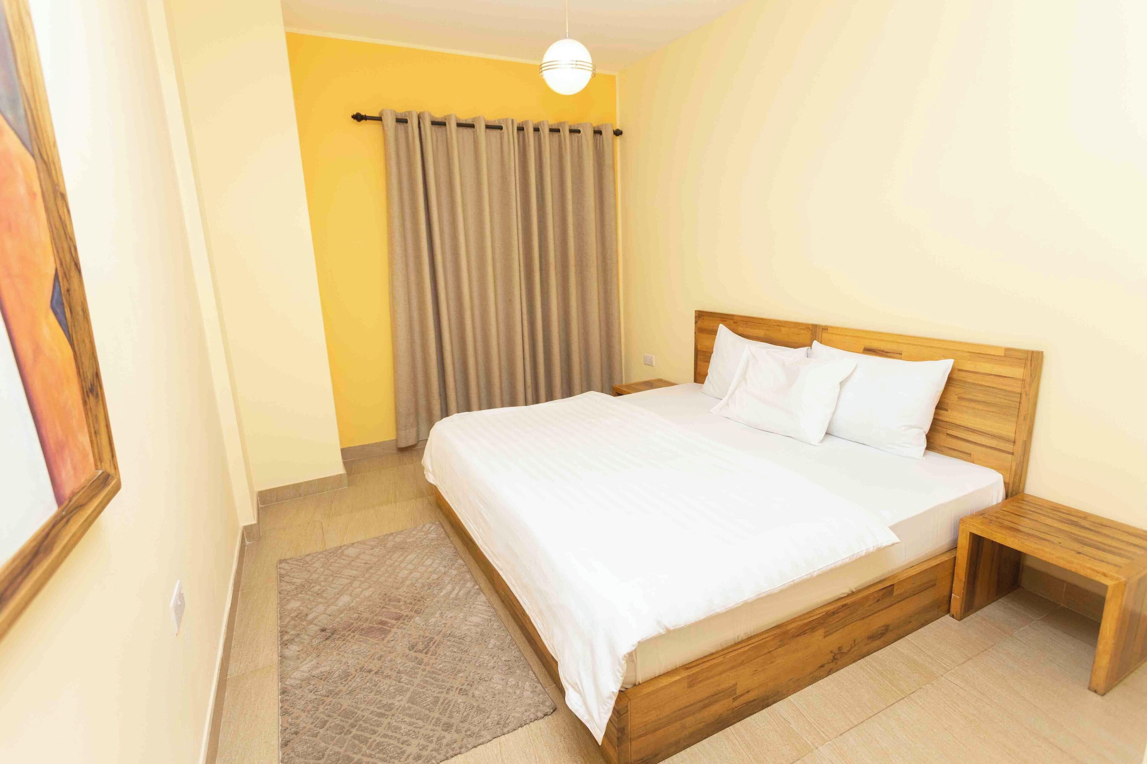 A bedroom with a wooden bed, a nightstand, a grey curtain, and a hanging light fixture.