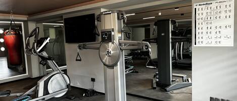 Un gimnasio con máquinas de cardio, un saco de boxeo y una pared de espejos con un cartel de NordicTrack.