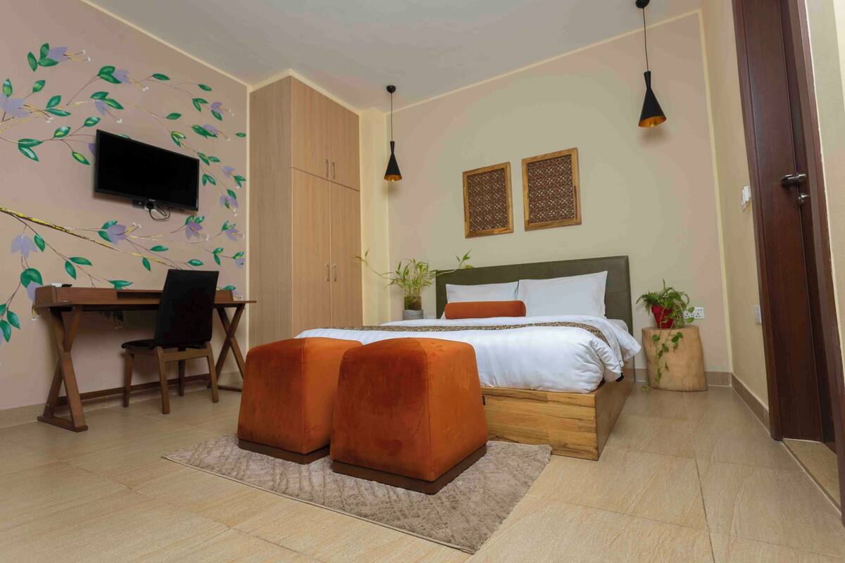 A bedroom with a bed, a desk, a TV, and a potted plant.