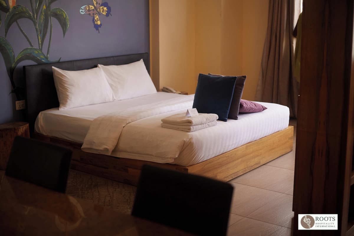 A neatly made bed with white and dark pillows, a folded towel, and a small sign on the bed.