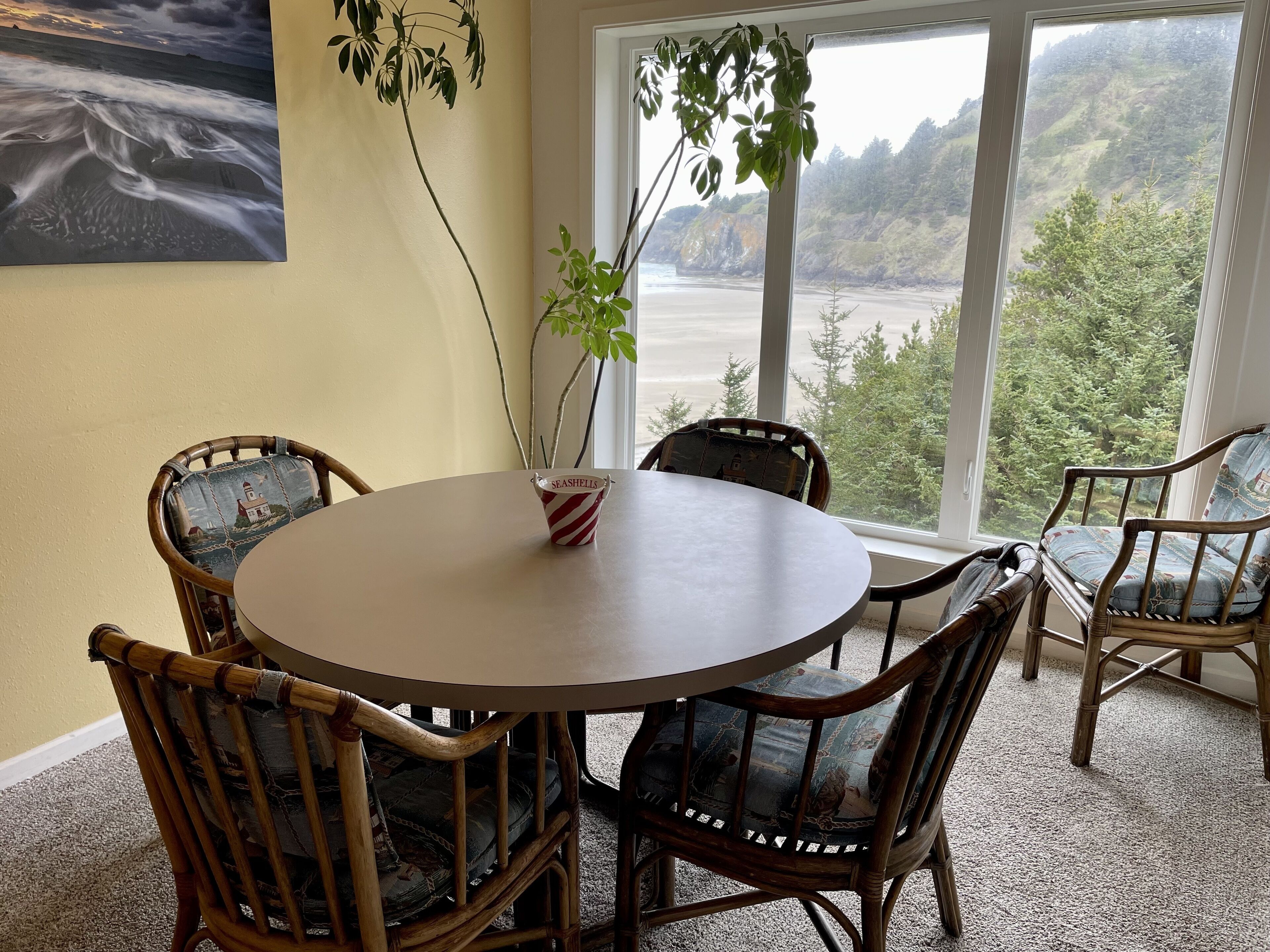 A round table with four chairs, a vase with a plant, and a painting on the wall.