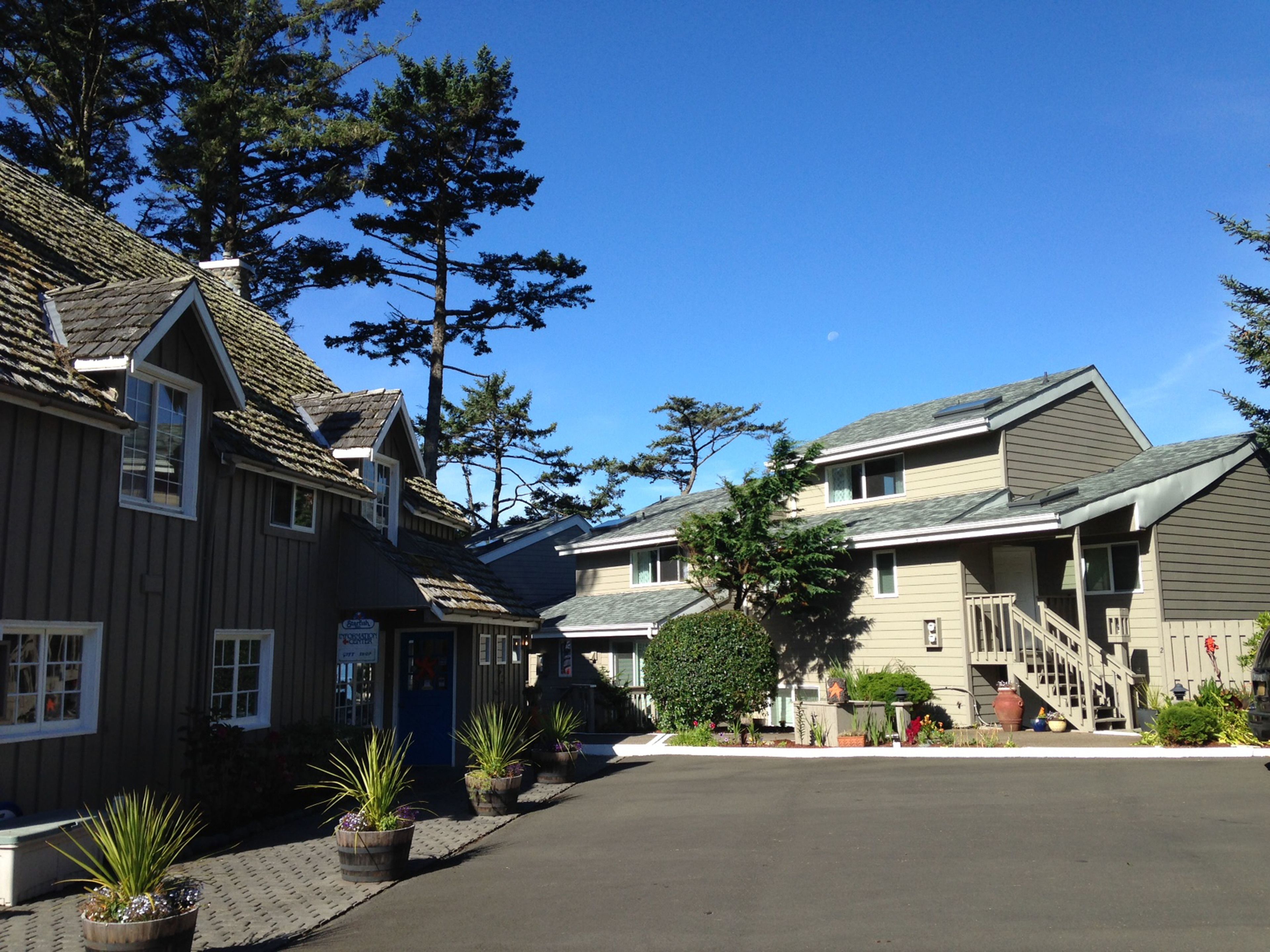 A row of two-story buildings with a central driveway, surrounded by trees and potted plants.