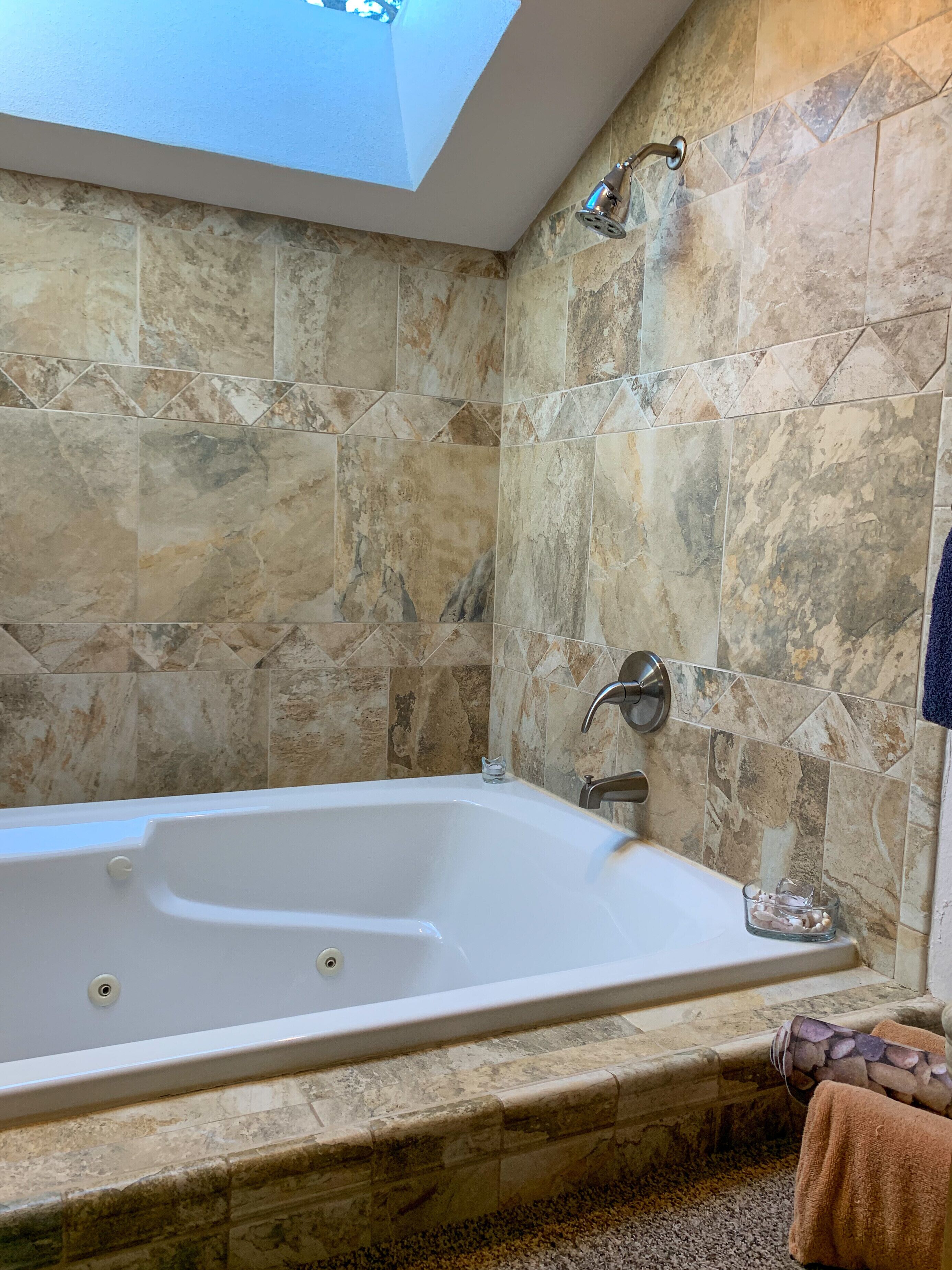 A bathroom with a freestanding bathtub, a skylight, and stone tiles.