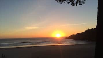 Ein Strand mit Sonnenuntergang, ruhiger See und felsiger Küste.
