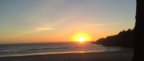 A beach with a sunset, calm sea, and a rocky coastline.