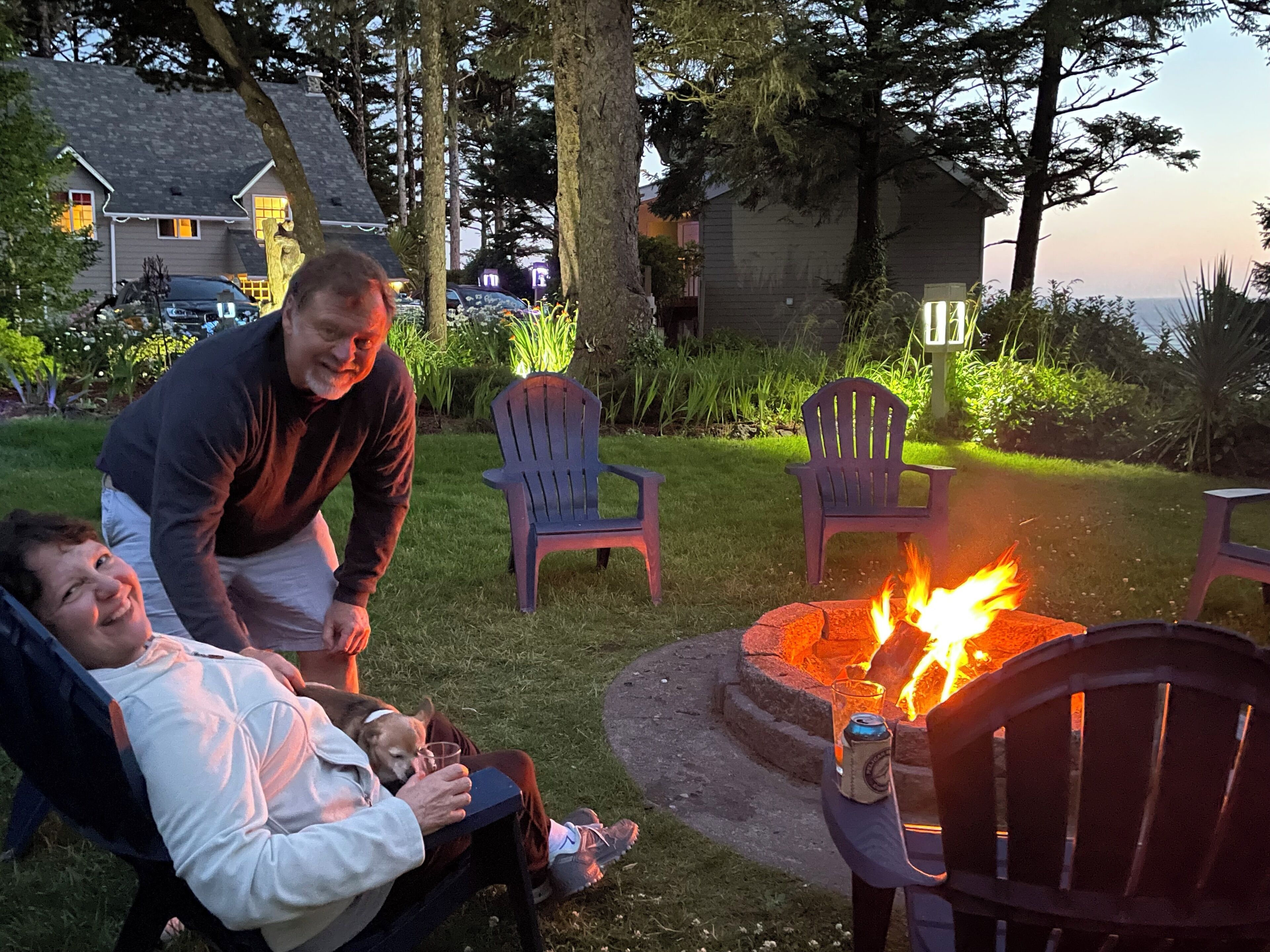 A patio area with a fire pit, outdoor seating, and a view of a house in the background.