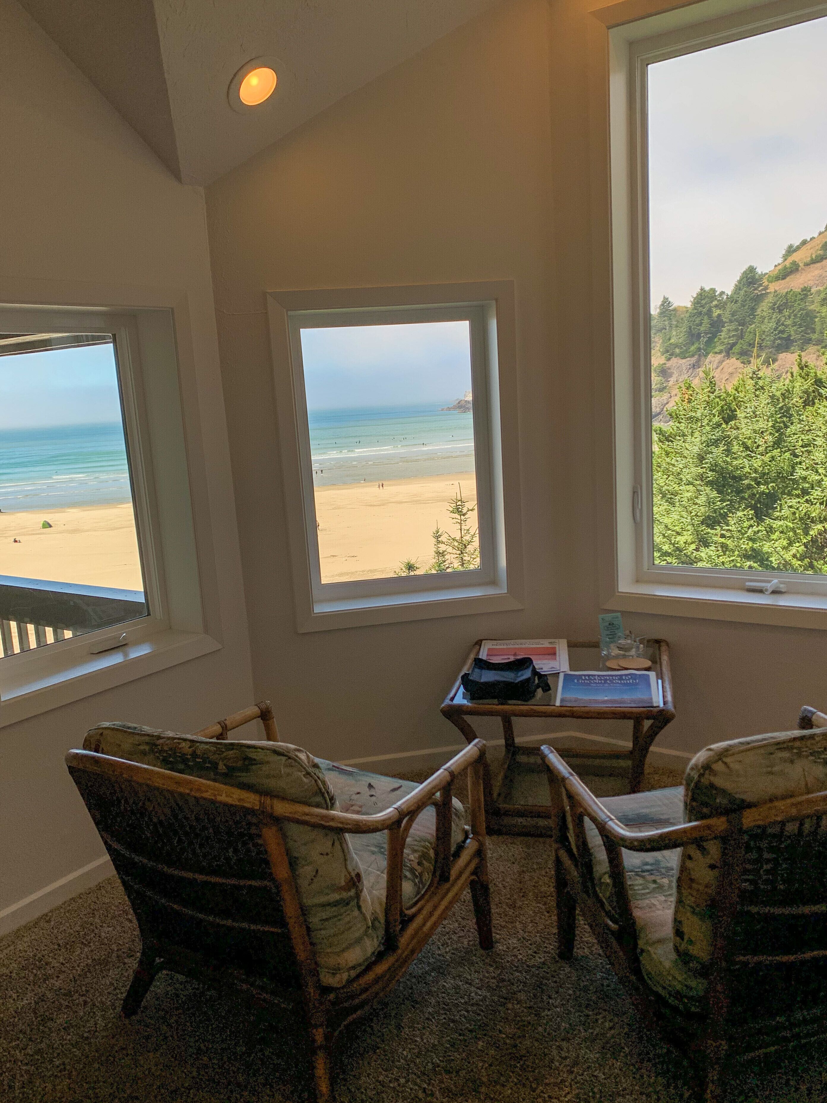 Una habitación con vistas a la playa, dos sillones de mimbre, una mesita y un ventanal con vistas al océano y las colinas.