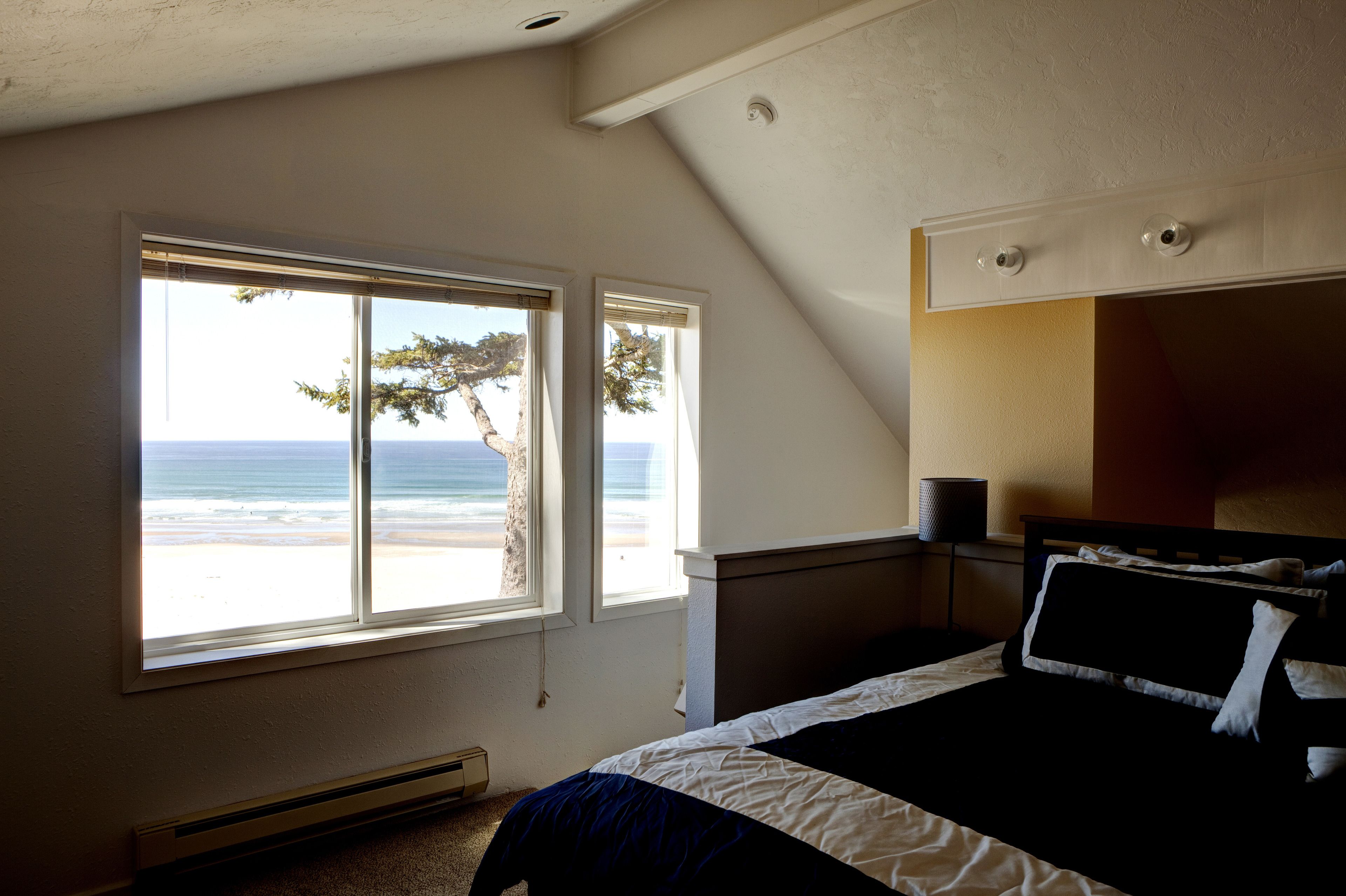 Ein Schlafzimmer mit großem Fenster und Meerblick, einem Bett und einem Nachttisch.