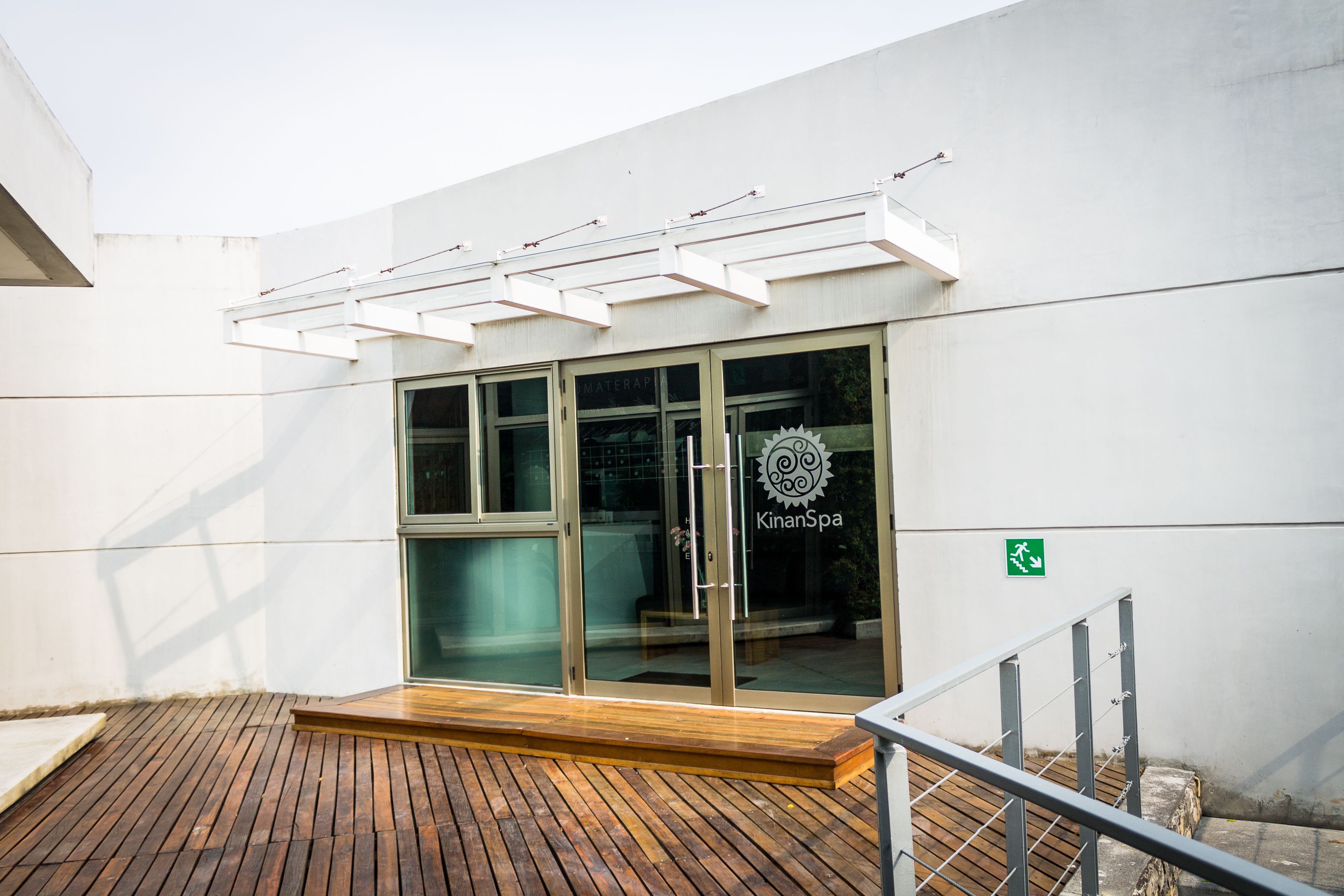 A modern building with a glass entrance, wooden deck, and a metal railing.