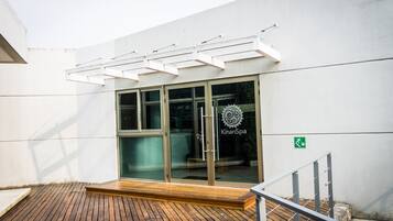 A modern building with a glass entrance, wooden deck, and a metal railing.