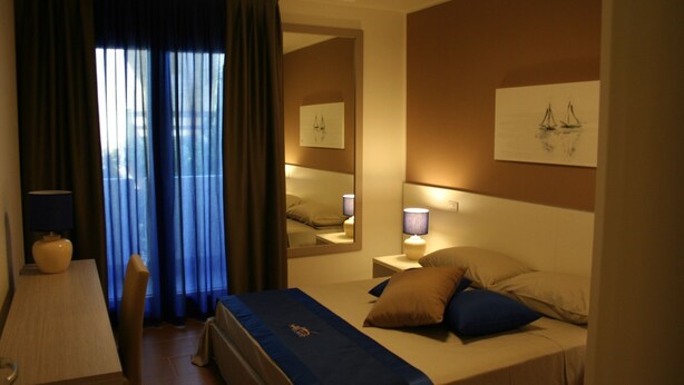 A hotel room with a bed, bedside lamps, a mirror, a window with curtains, and a painting on the wall. - Apart Hotel Atlantic (Grado)