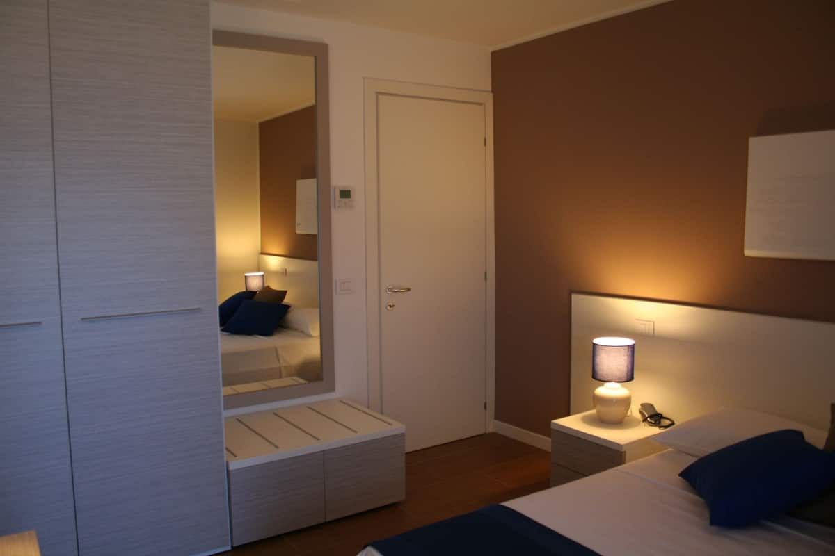 A hotel room with a bed, bedside table, lamp, and a wardrobe with a mirror.