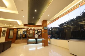 A modern hotel lobby with a reception desk, a staircase, and a large window offering a view of the outdoors. - Hotel Sai Grand Castle Inn (Rahata)
