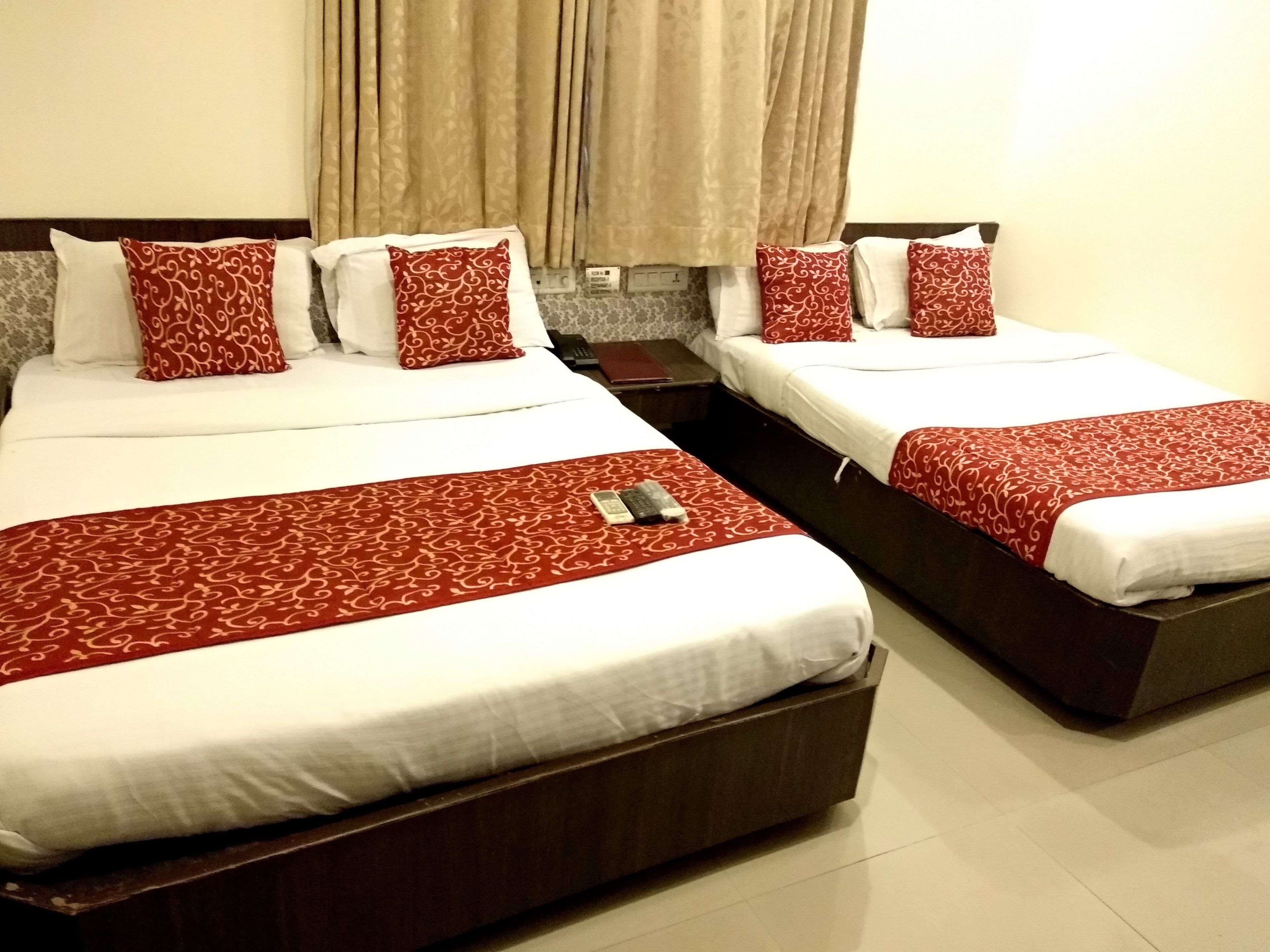 Two double beds with red and white bedding, a remote control on the bed, and a nightstand with a phone.